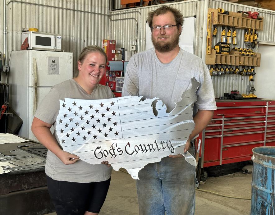 Amanda and Jacob Hartz pose with one of their popular gift items, a metal flag cut in the shape of the United States. Its among more than 100 customized products they’ve created since investing in their CNC machine in April. Lori Sorenson/Rock County Star Herald Photo