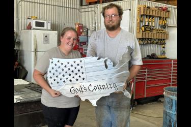 Amanda and Jacob Hartz pose with one of their popular gift items, a metal flag cut in the shape of the United States. Its among more than 100 customized products they’ve created since investing in their CNC machine in April. Lori Sorenson/Rock County Star Herald Photo