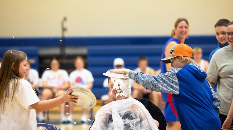 Bryan Bosch (seated) laughs as she is hit with pans of whipped cream by students Arya Tollefson (left) and Noah Engelkes. Samantha McGaffee/Rock County Star Herald Photo