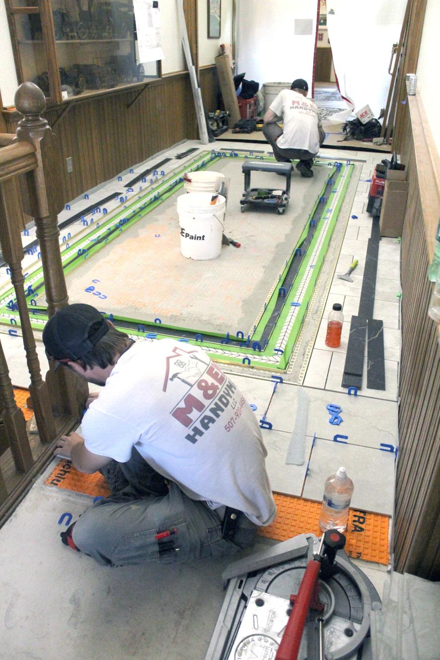 Matthew Sterrett (foreground), with M and Em Handyman LLC, places tile on the second floor of the Rock County Courthouse Thursday, May 22, with Joe Guy. The project is expected to be finished in a couple of weeks. The south end of the hallway is finished, allowing employees in the Land Records Office to move out of the Courthouse basement and back into their remodeled office space. Mavis Fodness/Rock County Star Herald Photo
