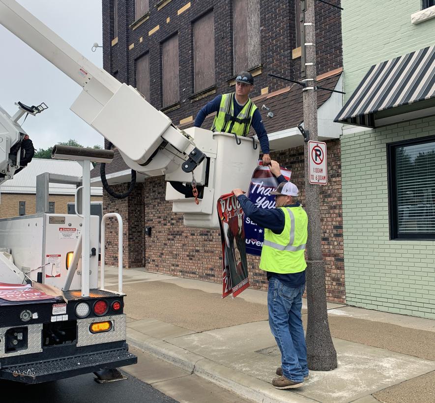 Missouri River Energy Services employee Mike Buss (right) exchanges vinyl banners with his coworker, Braydon Ripka, Tuesday, July 2, as the two remove the LHS Class of 2024 banners and hang new banners honoring local veterans. Mavis Fodness/Rock County Star Herald Photo