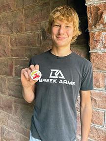 LHS sophomore Collin Knips holds one of the 2024 Tri-State Band Festival buttons featuring the design he completed as part of his high school art class. Submitted Photo