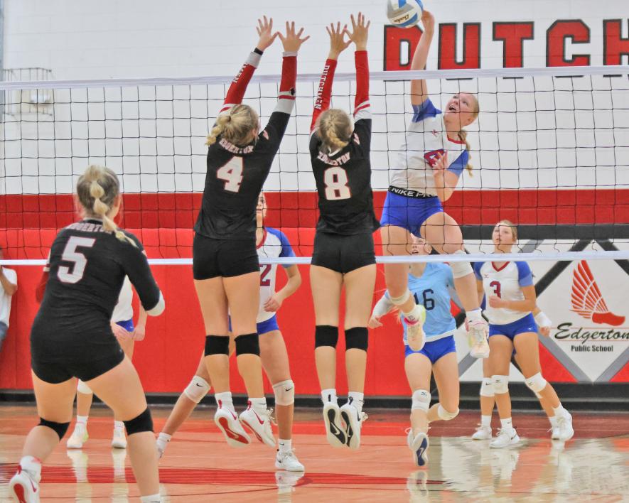 Freshman Brynn Bakken rises above the net to spike the ball against two Edgerton defenders. The Patriots lost the “Queens of the Court” three sets to one on Friday, Sept. 22, on the road.