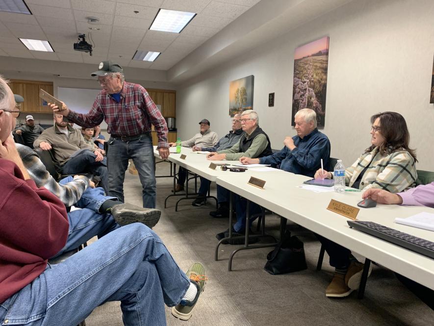 Paul Aukes holds a piece of angle iron with two bullet holes shot from a rifle to illustrate the possible danger of allowing rifles to be used to hunt deer in Rock County. Commissioners (at the table far right) conducted a listening session Tuesday night, Dec. 2, in the Rock County Library basement where 40 people attended. Mavis Fodness/Rock County Star Herald Photo