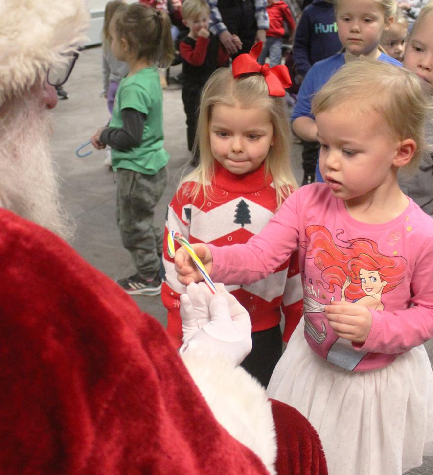 Santa Claus (Dave Siebenahler) hands a striped candy cane to Lainey Gath, 3, as Paisley Hanenburg, 4, watches. Mavis Fodness/Rock County Star Herald Photo