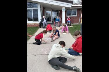 Residents (from left) Sonja Goembel, Marilyn DeBates and Anna Harrison enjoy watching the visiting sixth-graders create sidewalk art with colorful chalk. Students are (from foreground to back) Jack Bailey, Levi Baker, Harper Hulstein, DesiRae Miller, Lucy Knips, Avery Van’t Hof and Sydney Van Grootheest. Lori Sorenson/Rock County Star Herald Photo