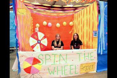 Junior Bethany Behr (left) and Rayann Remme earned second place in the booth decorating contest with their "Spin the Wheel" booth in the high school gym during Winter Carnival. Greg Hoogeveen/Rock County Star Herald Photo